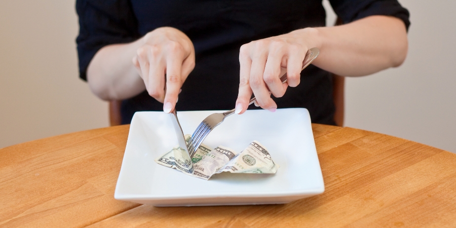 A plate with a $5 bill sitting on a table, and someone is pretending to eat it with a fork and knife