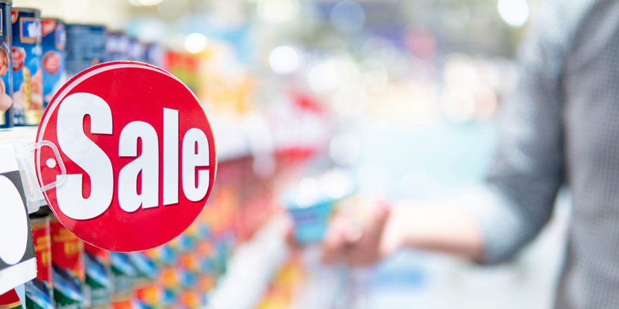 Red sale label on product shelf in supermarket with blurred male shopper choosing food package in the background. shopping lifestyle in grocery store concept