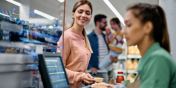 Happy woman checking out at grocery store with woman operating the checkout slightly blurry, focusing on screen