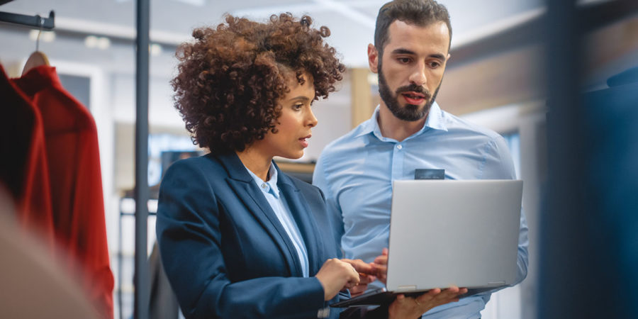 Clothing Store: Businesswoman Uses Laptop Computer, Talks to Visual Merchandising Specialist, Collaborate To Create Stylish Collection. Small Business Fashion Shop Sales Manager Talks to Designer.